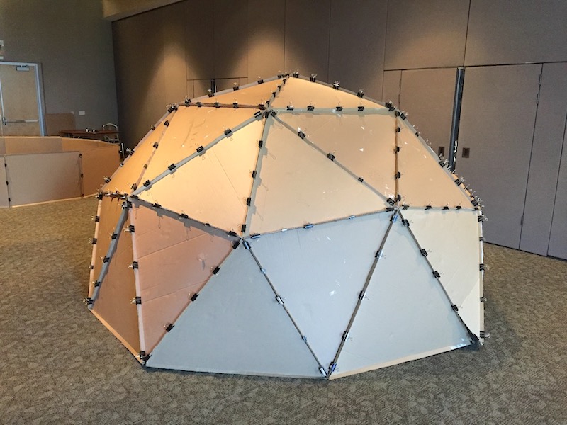 A cardboard geodesic dome, resting on the floor